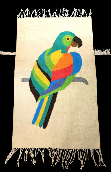 A rectangular cream-colored woven textile with fringe on the top and bottom edges, featuring a colorful parrot design in the center. The parrot illustration includes green, blue, yellow, orange, and red sections, set against a solid black background.