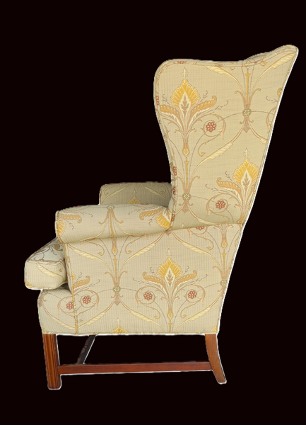 A high-back wingback armchair upholstered in a warm beige fabric with a yellow and gold botanical scroll pattern, supported by dark brown wooden legs, shown against a solid black background.